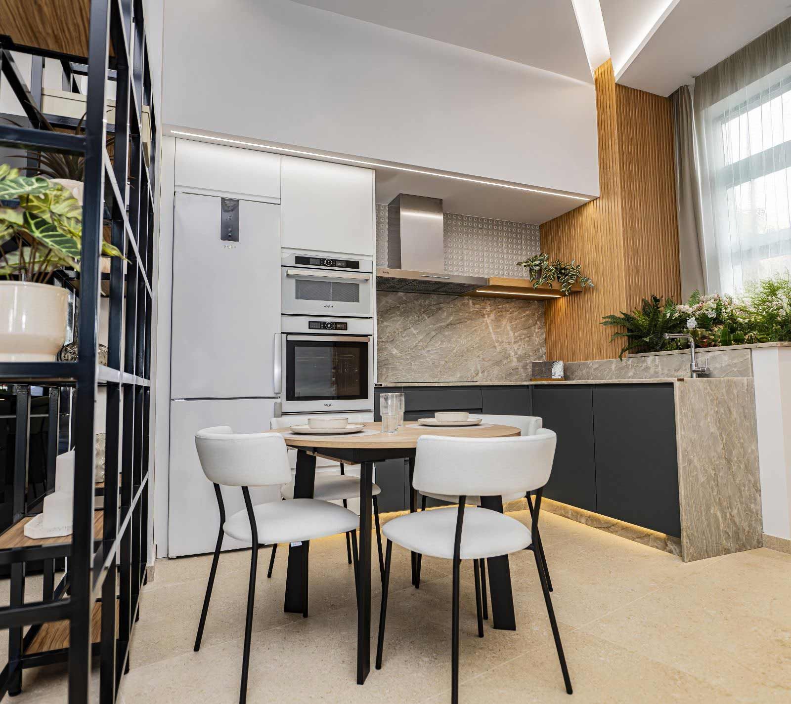 Cocina moderna con electrodomésticos blancos, gabinetes oscuros, mesa redonda y sillas.