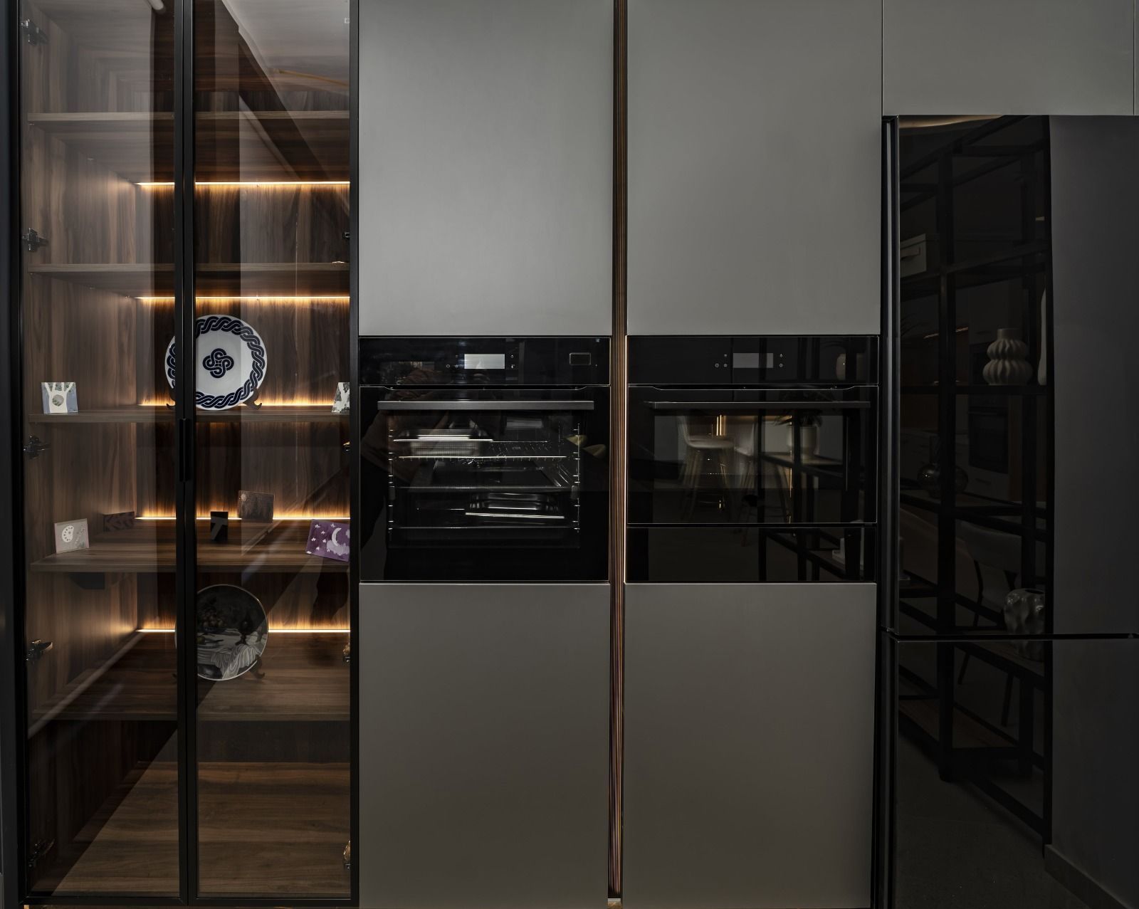 Muebles de cocina empotrados en color gris oscuro con horno, vitrina con estantes iluminados y diseño moderno.