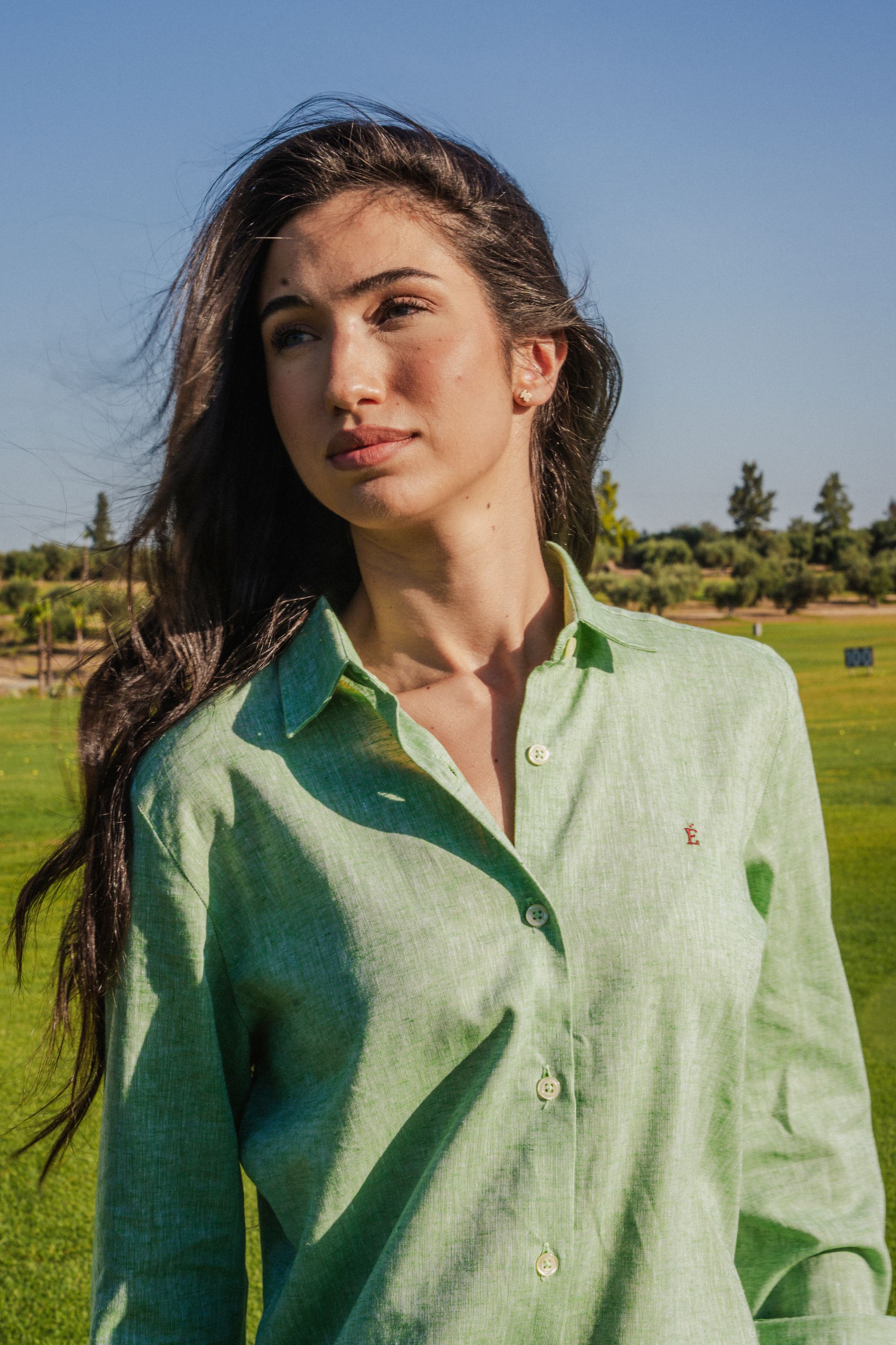Una mujer con una camisa verde y pantalones negros está parada frente a unas palmeras.