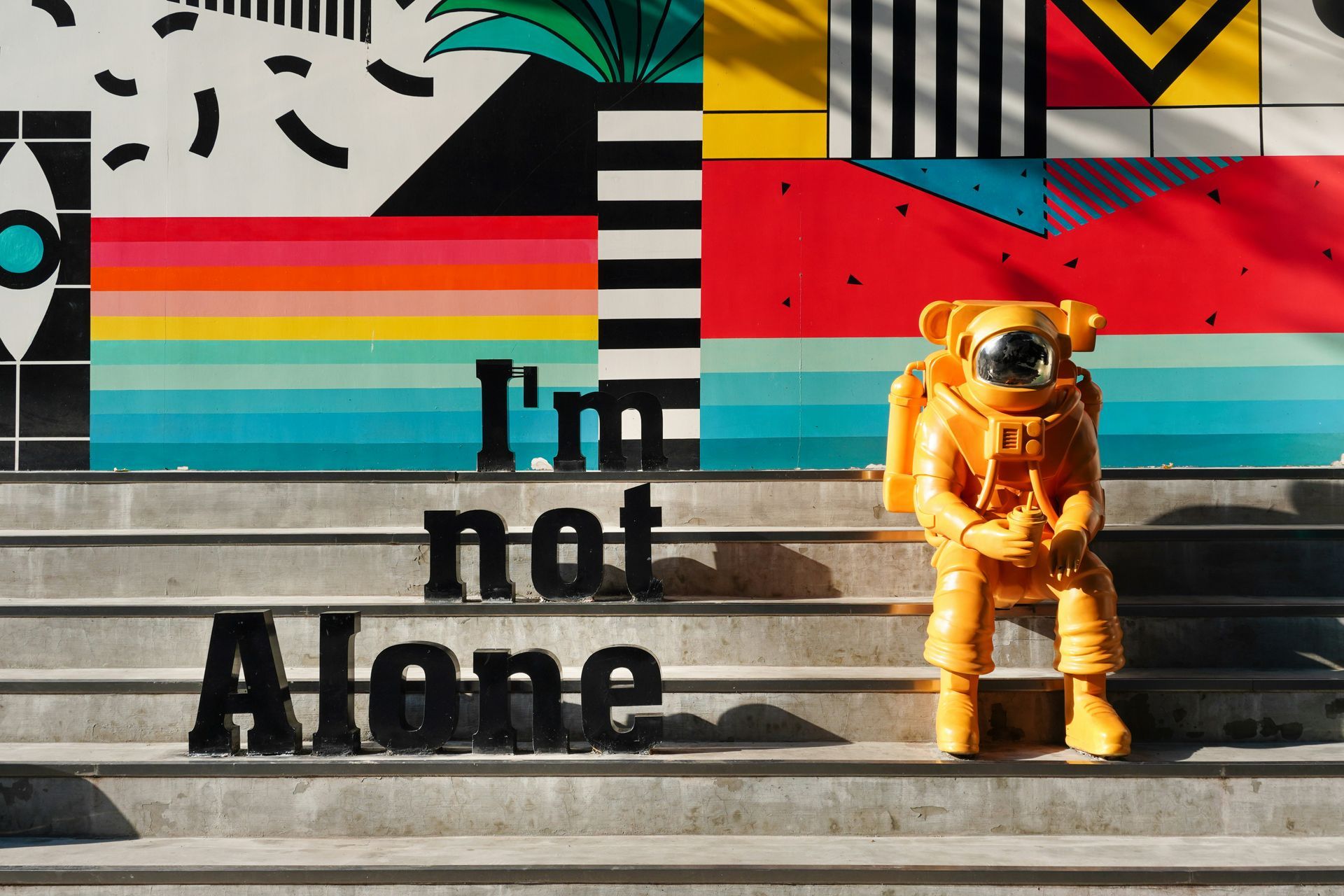 Ein Astronaut auf der Treppe sitzend mit buntem Hintergrund und Textbausteine: I'm not Alone