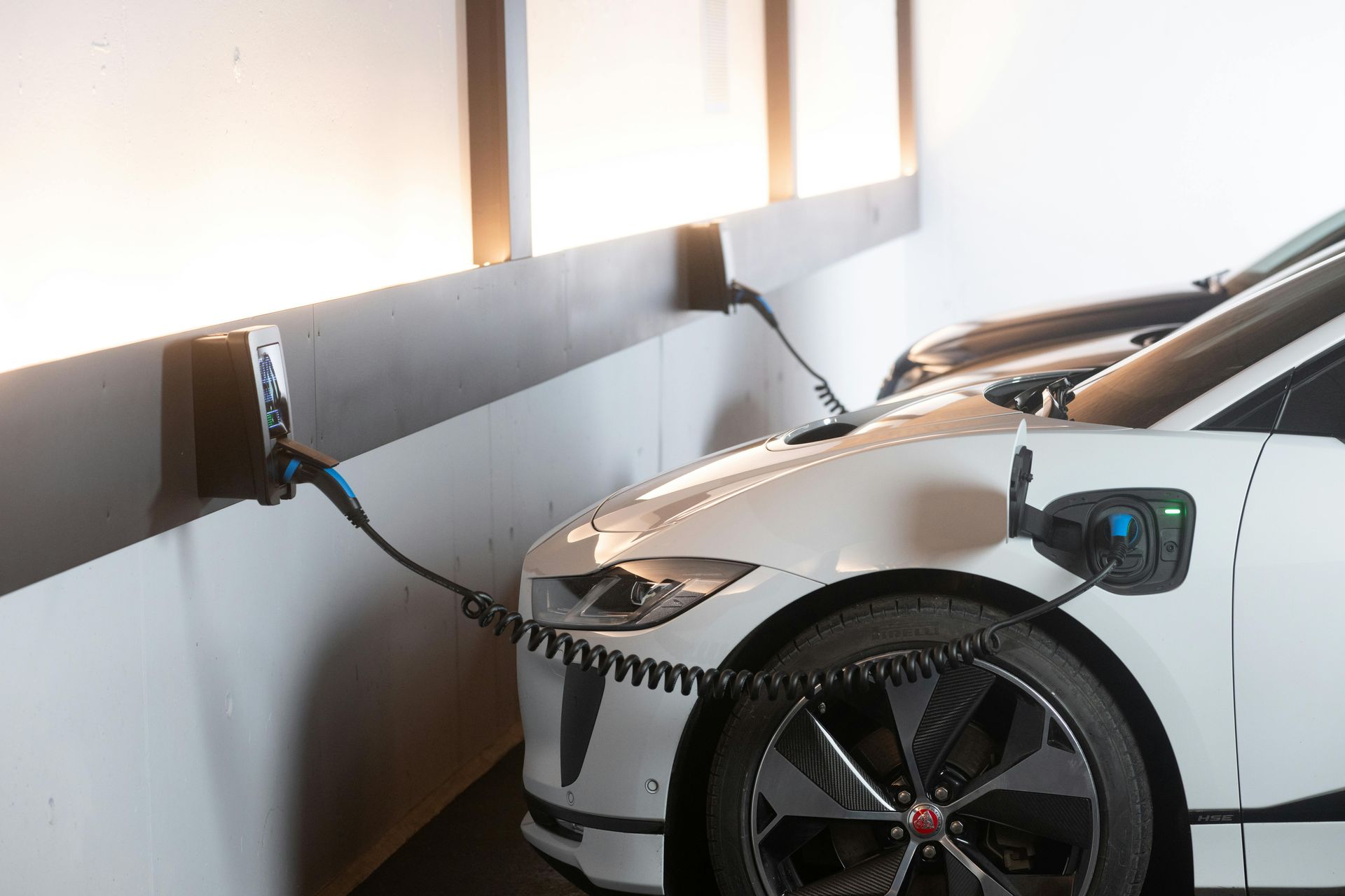 Valkoisen sähköauton latausasema autotallissa seinälle asennetulla latauspisteellä