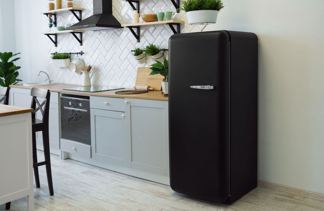 Réfrigérateur rétro noir dans une cuisine lumineuse avec des accents blancs et bois.