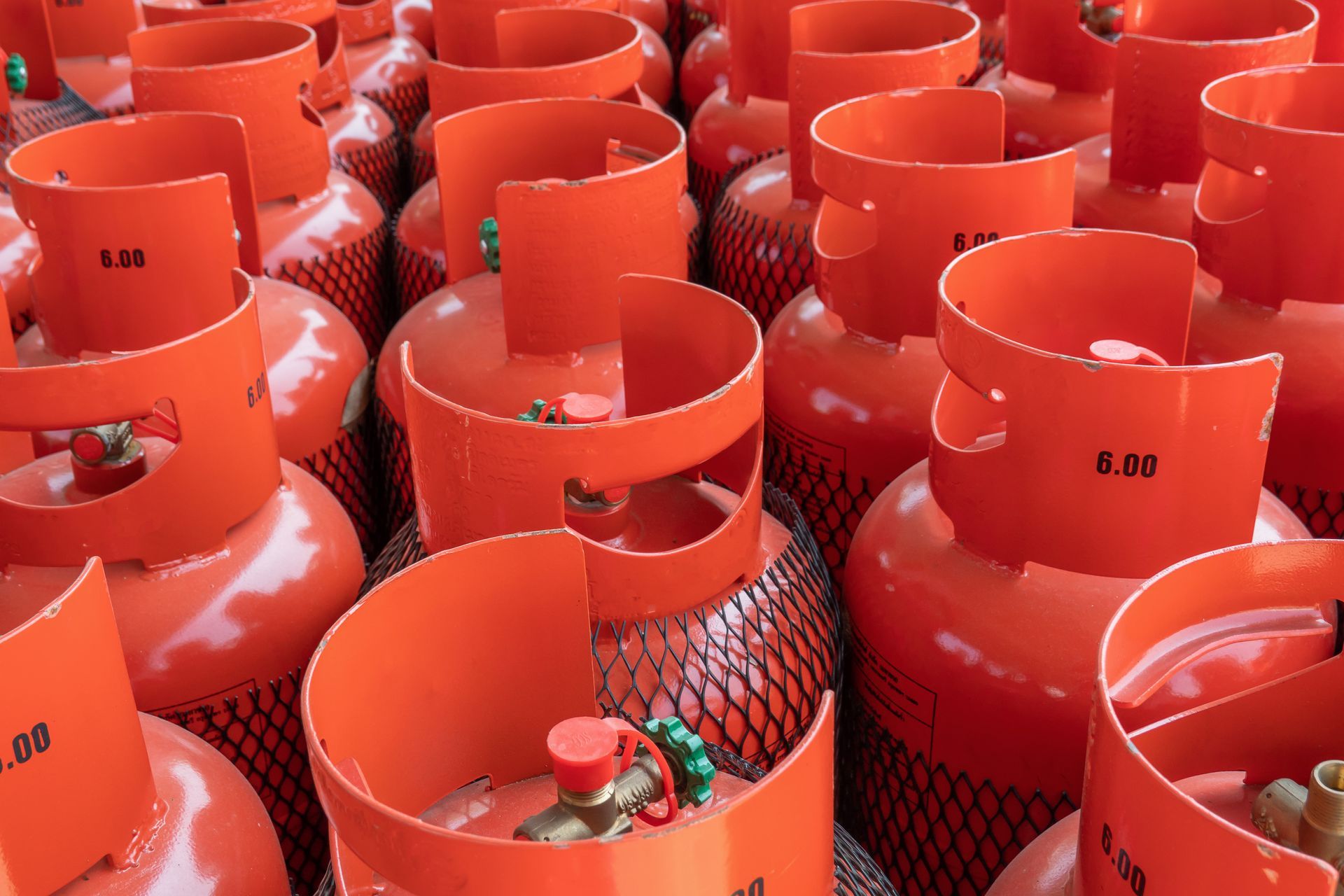 Réservoirs de propane orange, vue rapprochée, à l'extérieur, plusieurs en groupe, avec poignées supérieures ouvertes.
