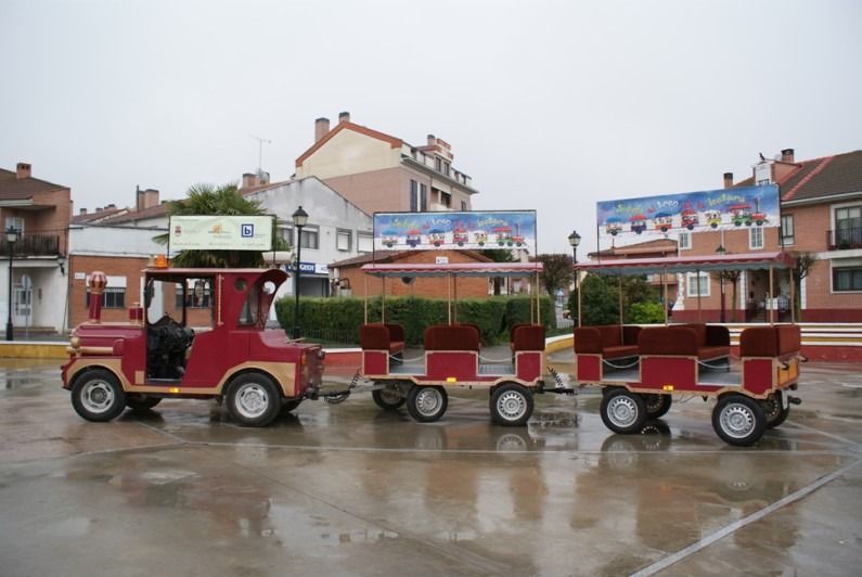 Un jeep rojo con un tren atado a él está estacionado en un estacionamiento.