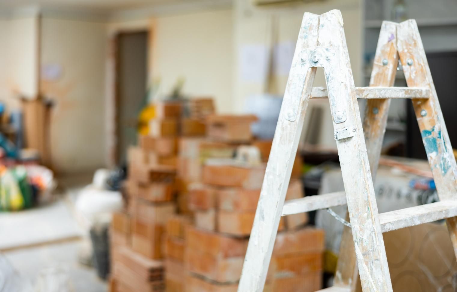 Escalera blanca en una habitación borrosa en obras, con ladrillos apilados y herramientas al fondo.