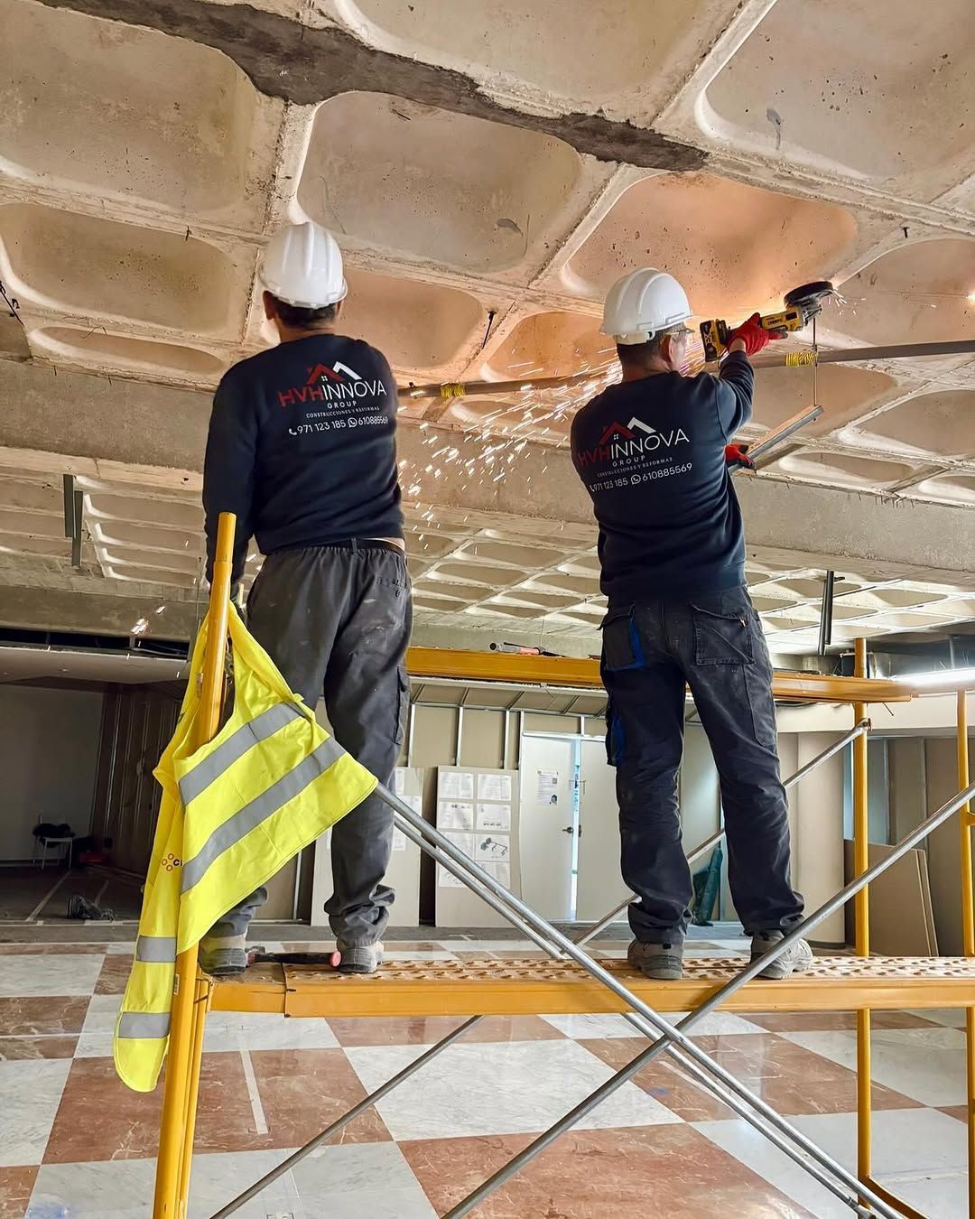 Dos trabajadores en andamios aplican aislamiento térmico con espuma en un techo de una habitación en renovación.