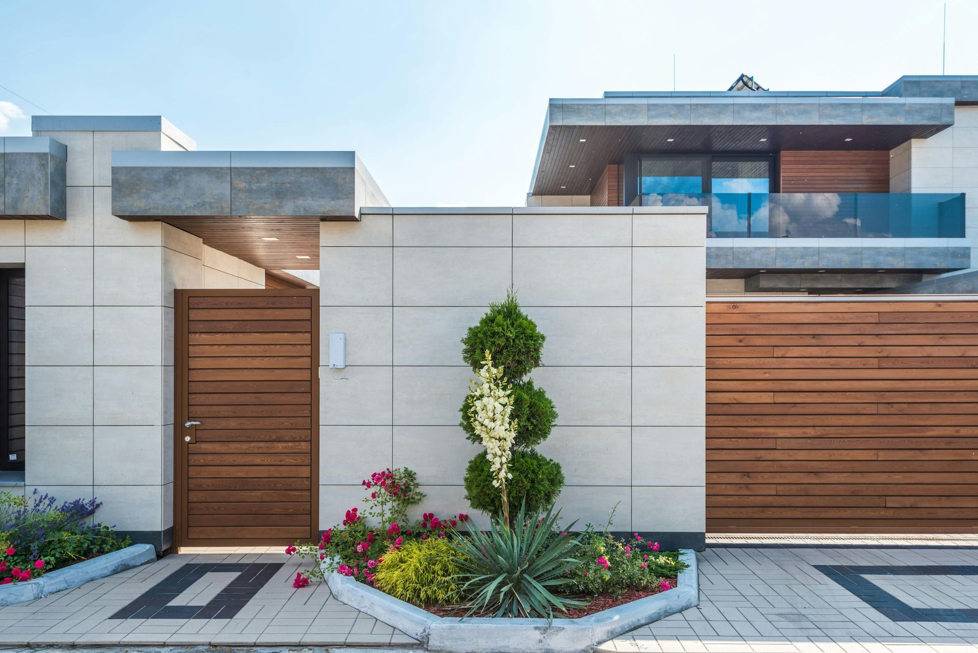 Exterior de casa moderna con garaje y puertas de entrada de madera, fachada de piedra y parterres ajardinados.