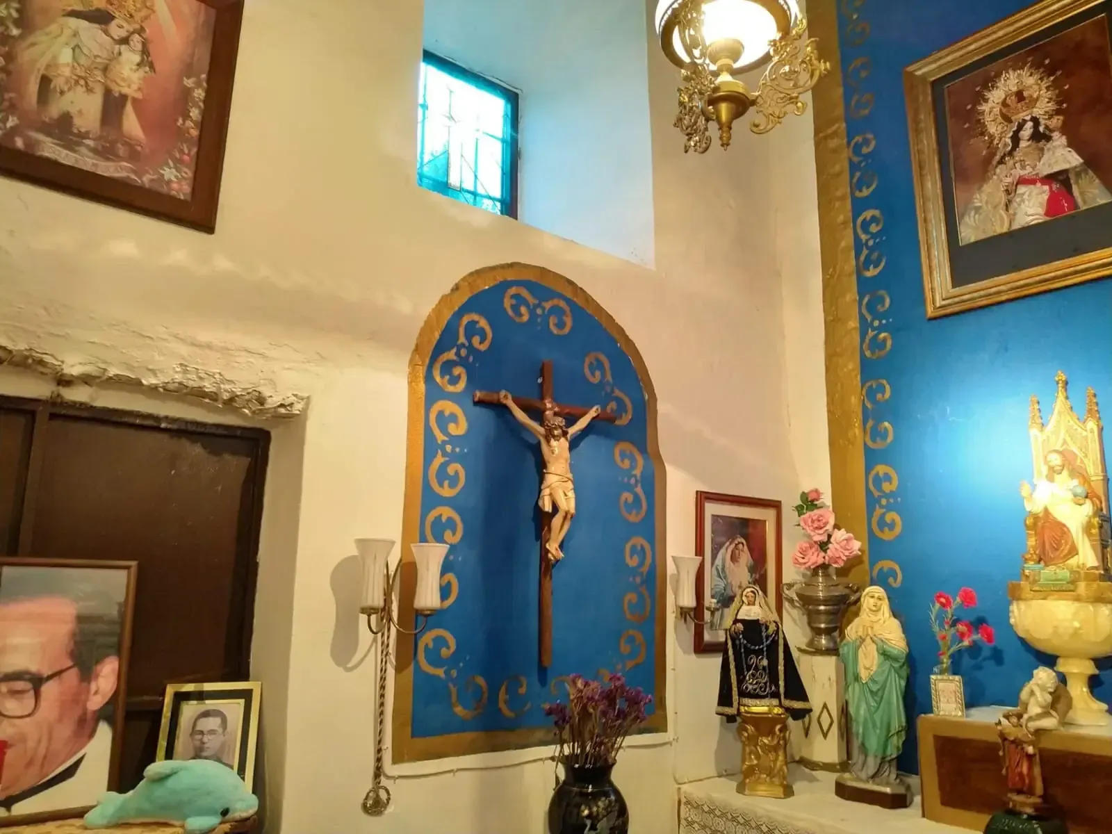 Interior de una capilla con un crucifijo, obras de arte religioso y elementos decorativos en azul y dorado.