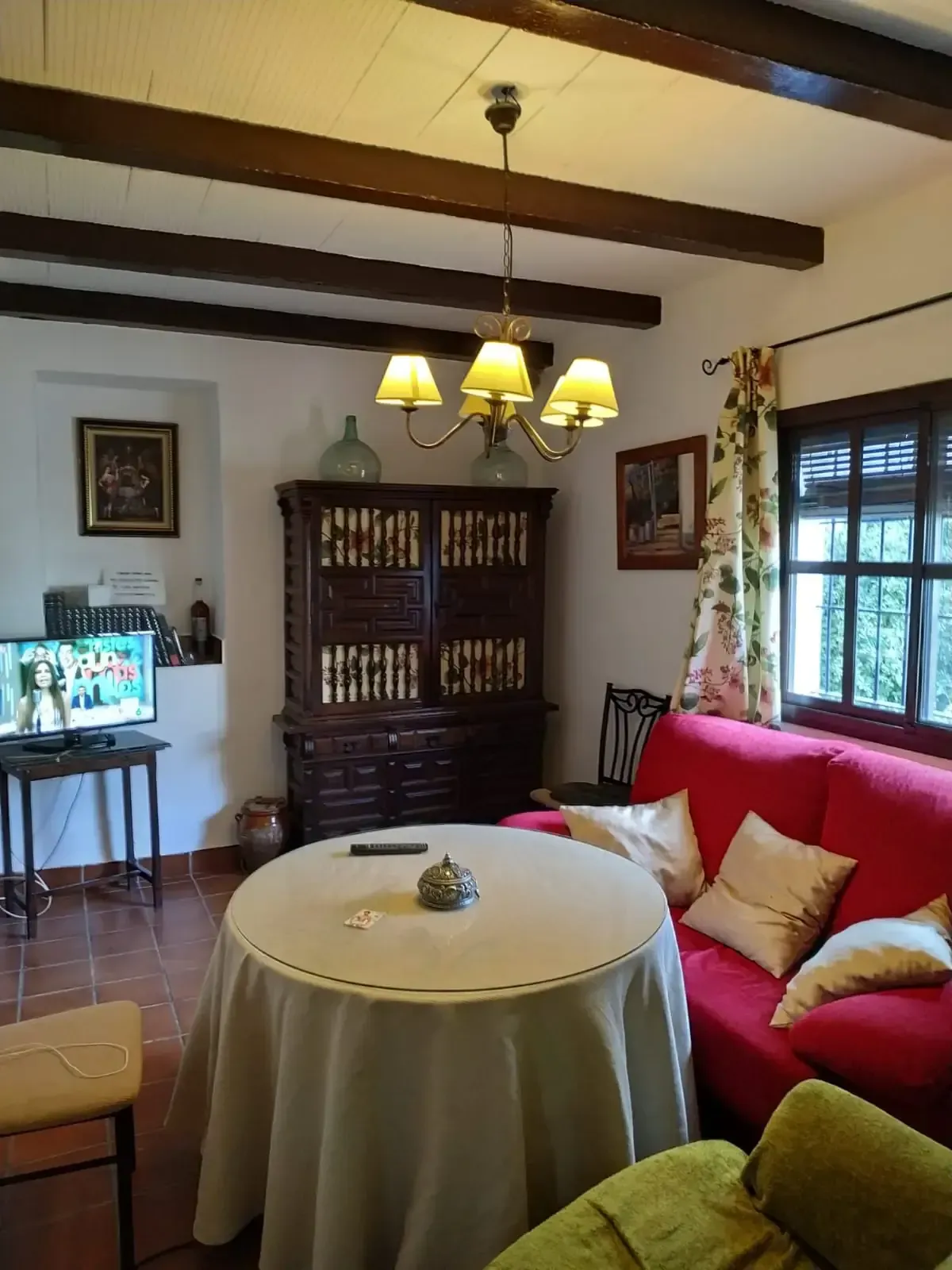 Acogedora sala de estar con un sofá rojo, mesa redonda, mueble antiguo y lámpara de araña.