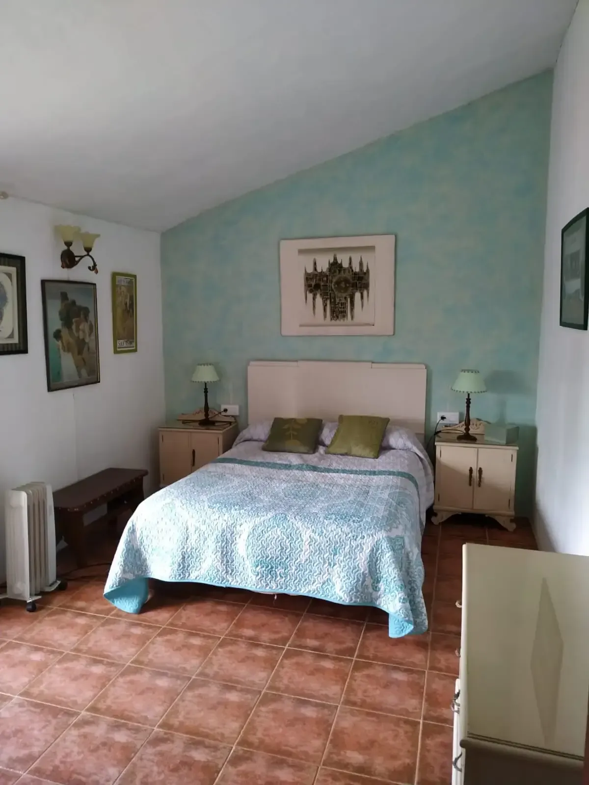 Dormitorio con pared con acento azul, cama doble, mesas de noche con lámparas y obras de arte.
