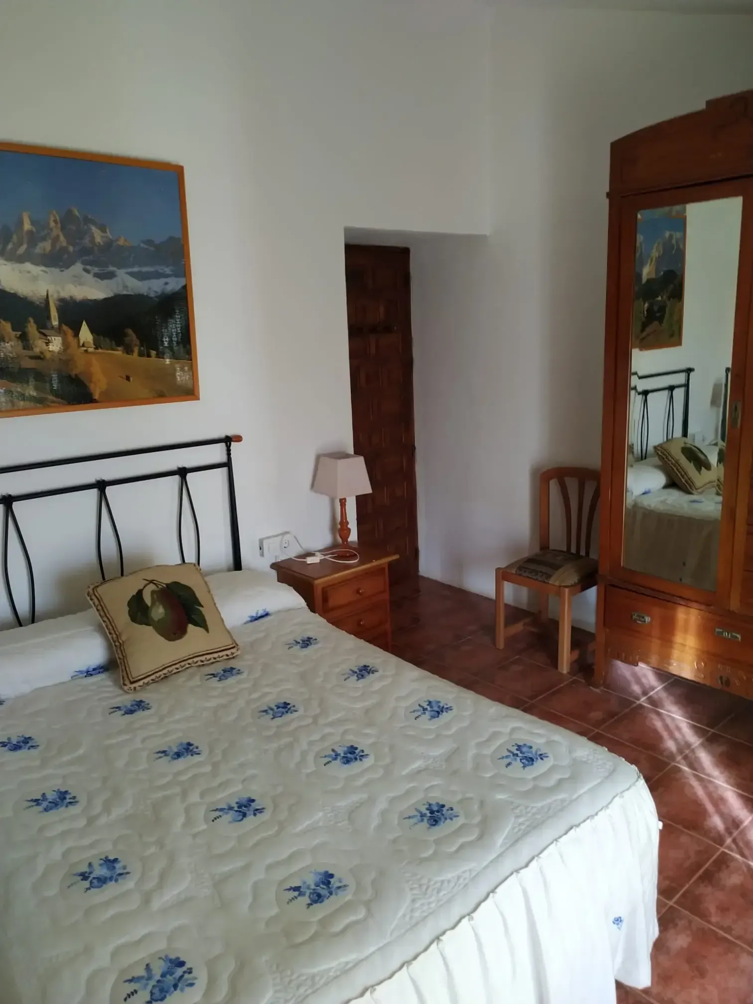 Dormitorio con cama, armario antiguo con espejo, cuadro, lámpara, silla y puerta.