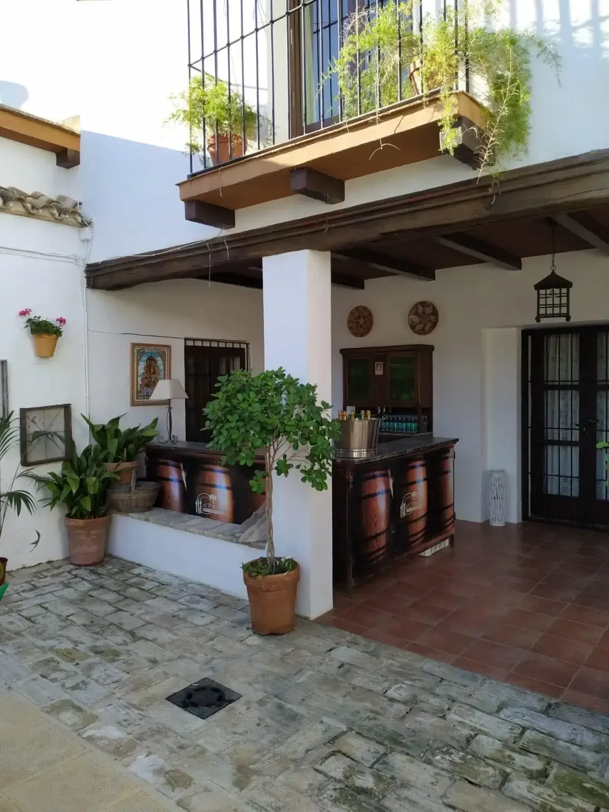 Patio con bar, plantas y balcón en el segundo piso. Paredes blancas, azulejos rojos y detalles en madera.