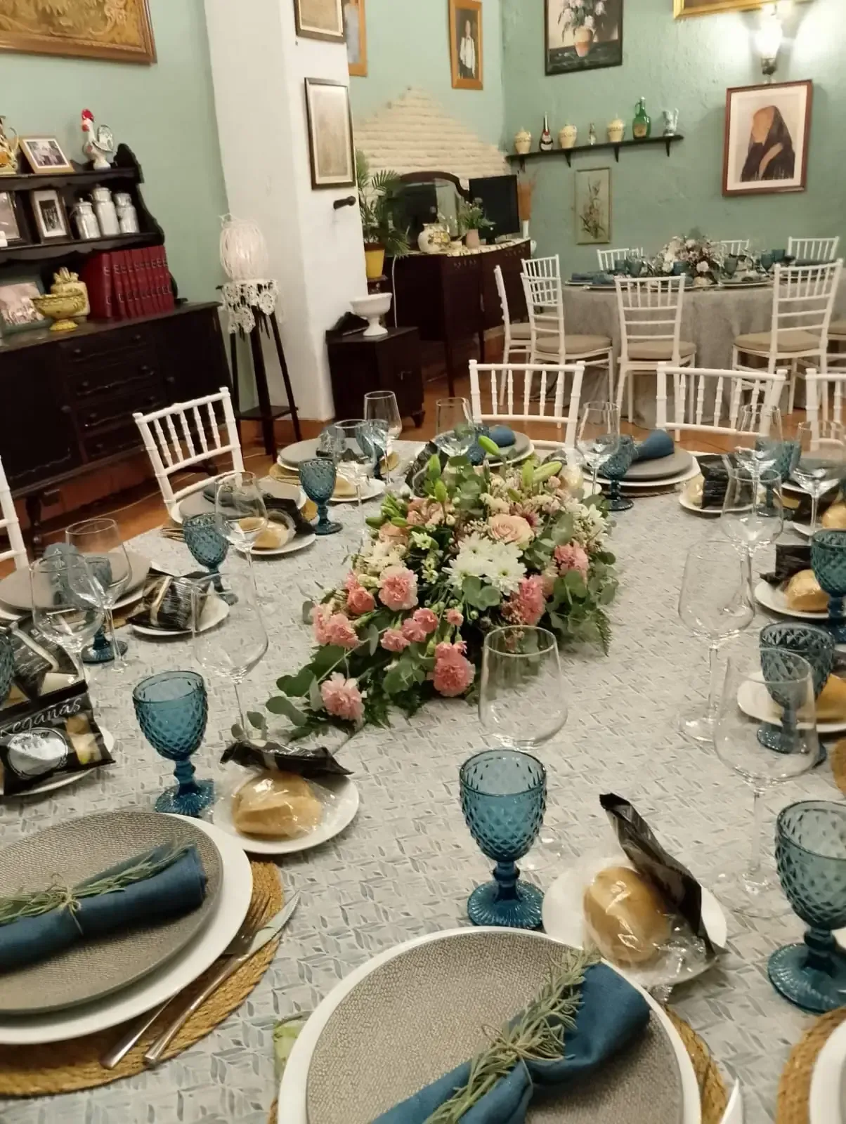 Mesa formal con centro de mesa floral, copas azules y sillas en un comedor vintage.