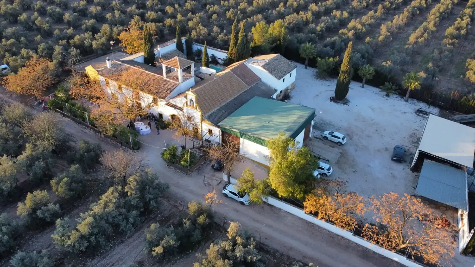 Vista aérea de una casa de campo española con olivos. Los edificios tienen paredes blancas y techos de tejas marrones.