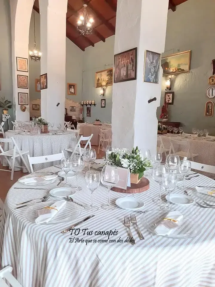 Elegante comedor, mesas dispuestas con mantelería blanca y rayada, flores y arte en las paredes.