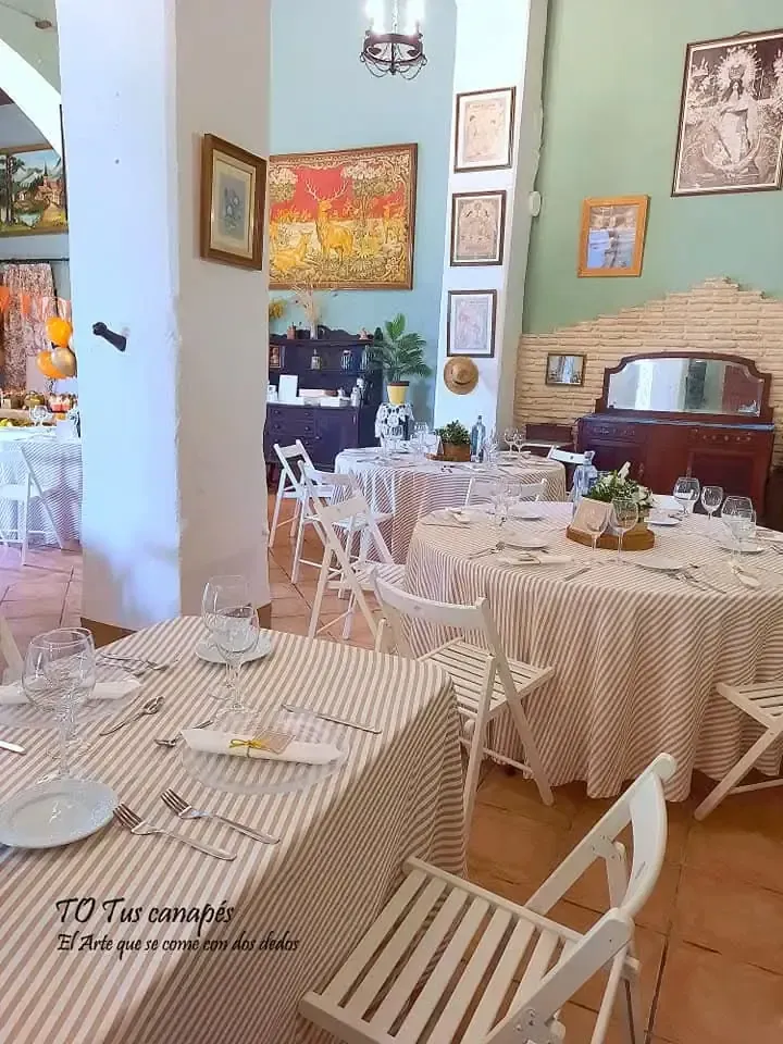Interior de restaurante con mesas redondas cubiertas con manteles a rayas y sillas plegables blancas.
