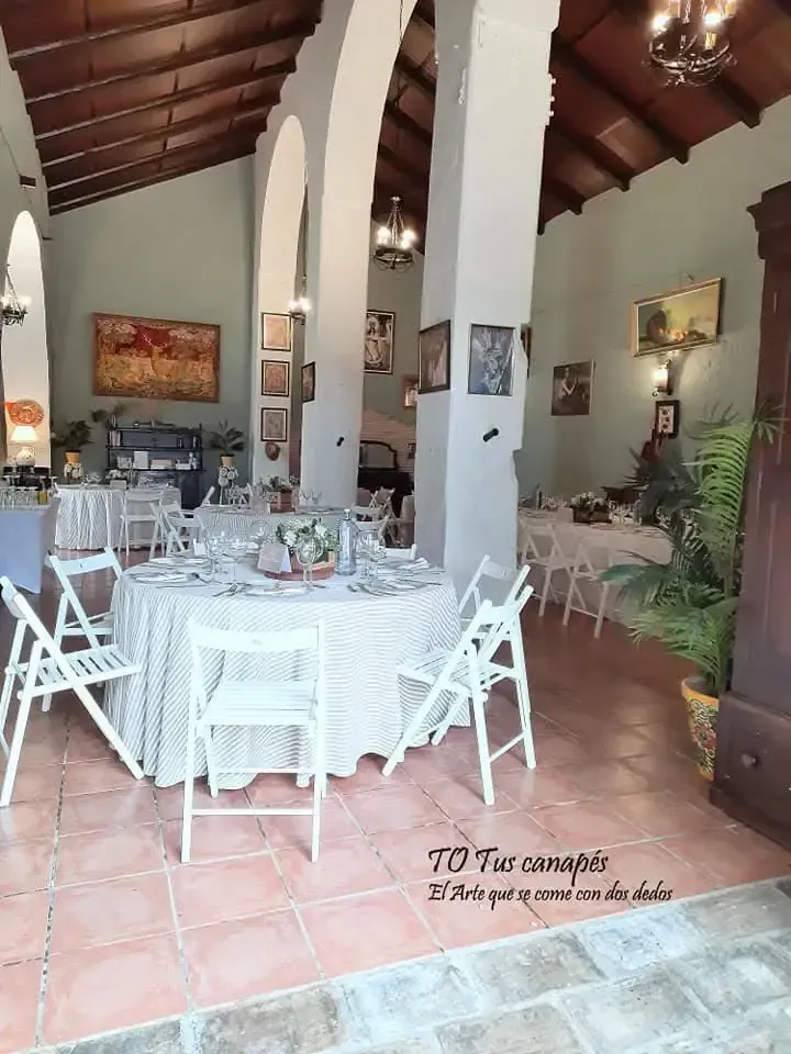 Comedor interior con mesas redondas, sillas plegables blancas y obras de arte.