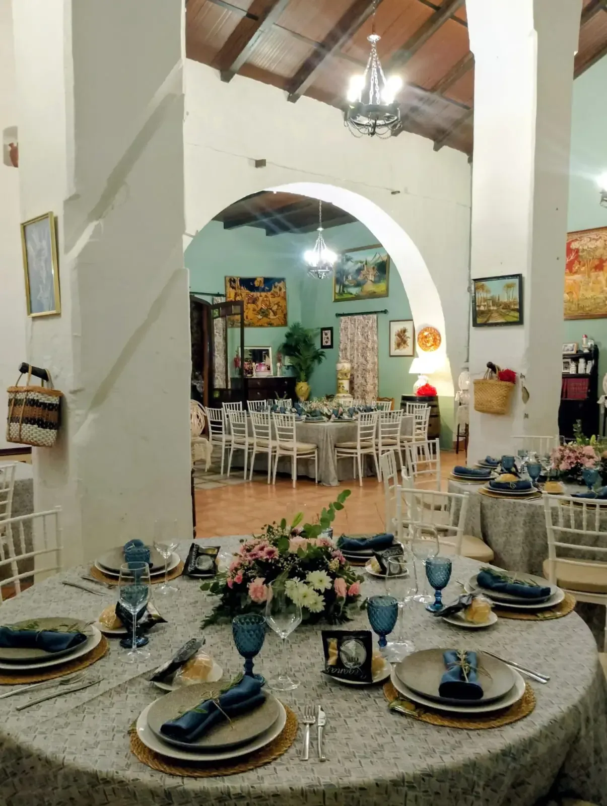 Elegante comedor con mesas preparadas. Manteles azul pálido, centros de mesa con flores, puertas arqueadas.