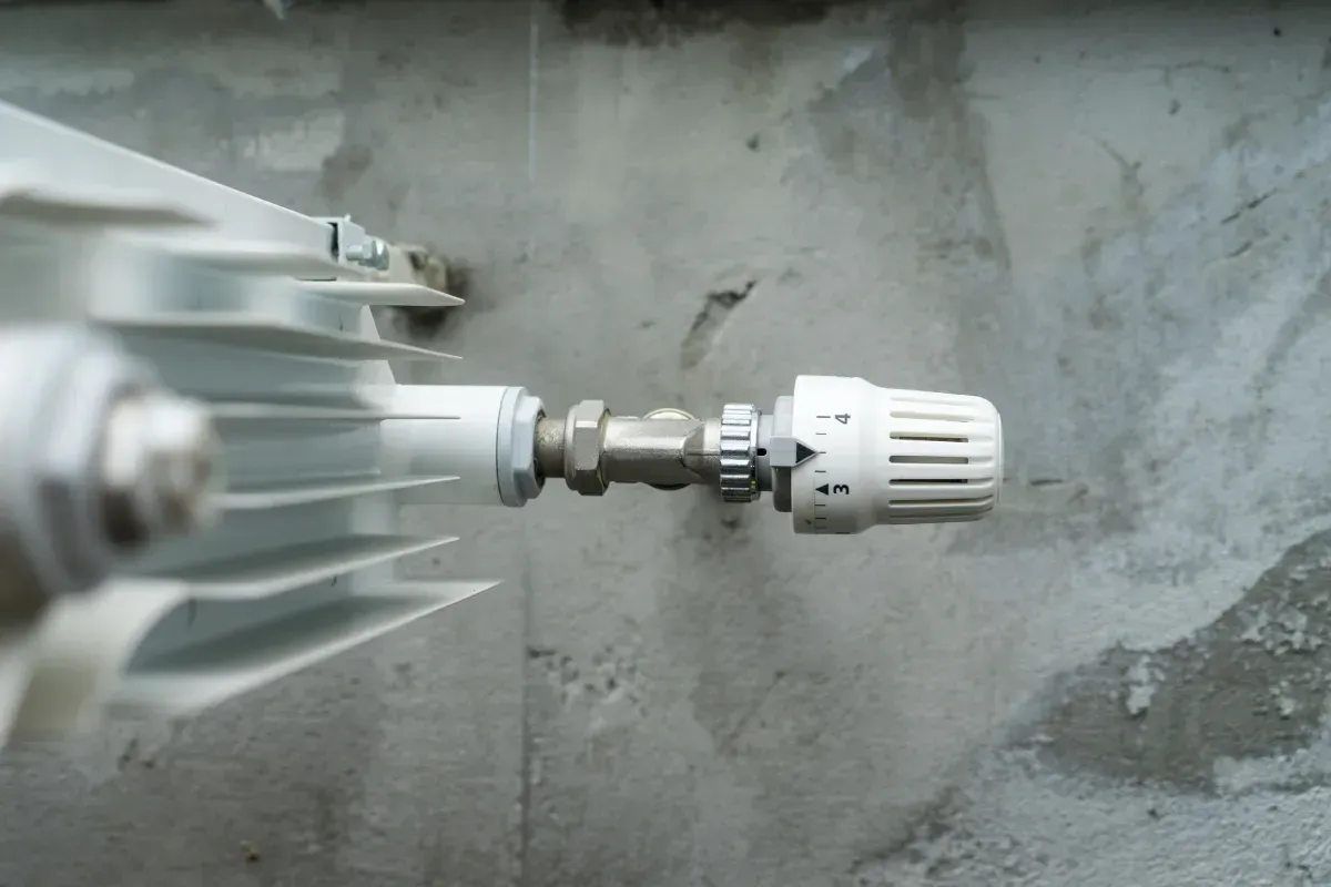 Radiador blanco con válvula de control de temperatura contra una pared de hormigón.