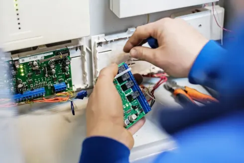 Persona con camisa azul trabajando en placas de circuitos electrónicos con herramientas.