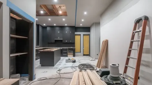 Cocina en remodelación con gabinetes oscuros, estantes abiertos y una escalera.