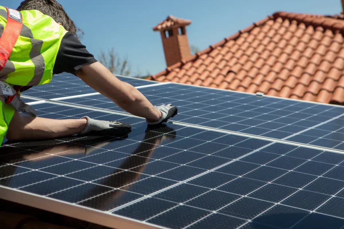Persona instalando paneles solares en un tejado, vistiendo un chaleco de seguridad.
