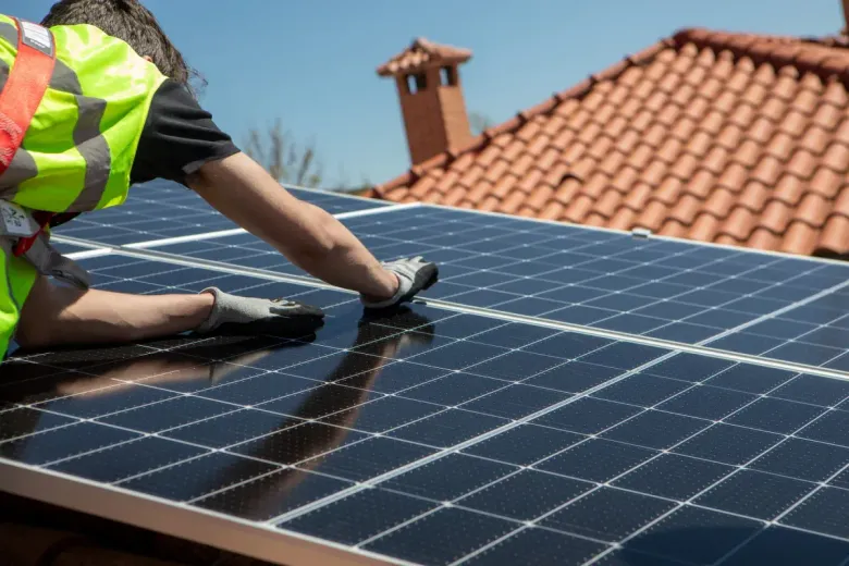Persona instalando paneles solares en un tejado, vistiendo un chaleco de seguridad.