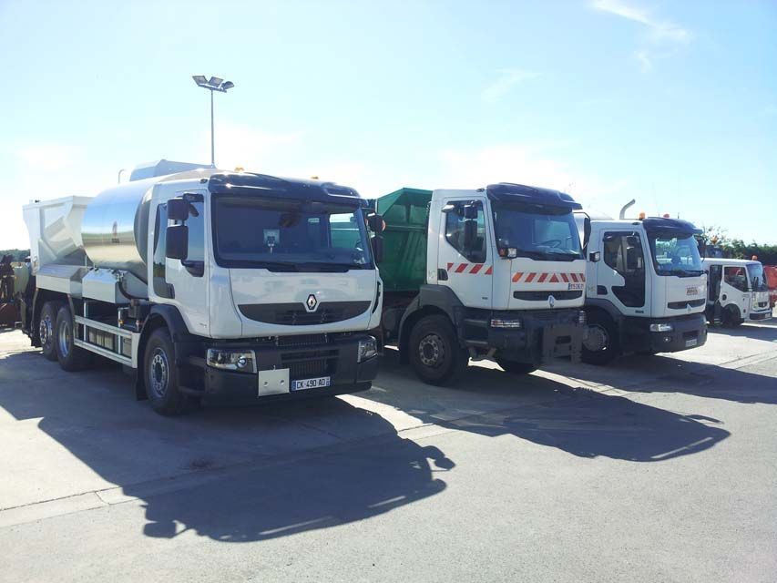 Trois camions Renault blancs garés sur un parking goudronné par une journée ensoleillée.