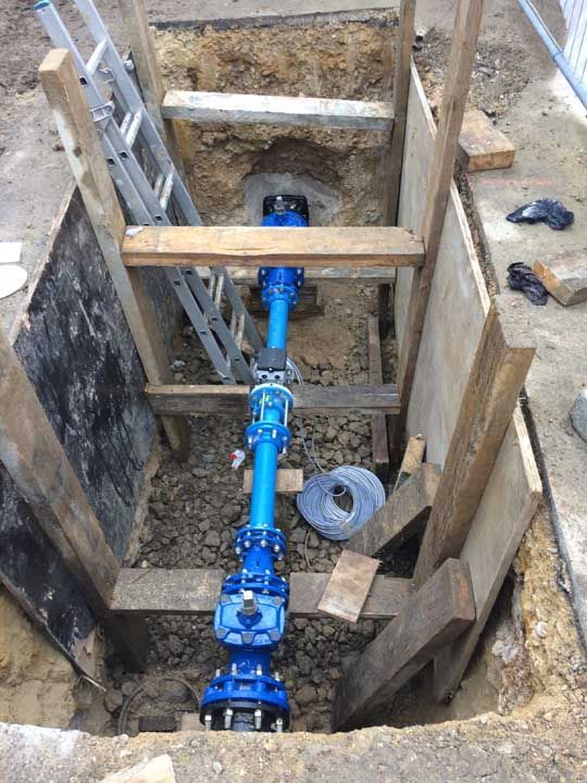 Section de tuyau d'eau bleu dans une tranchée de construction, soutenue par des étais en bois et une échelle.