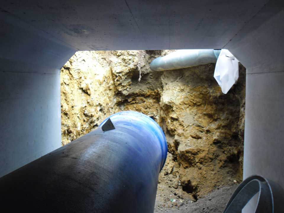 Gros tuyau dans une ouverture rectangulaire, face à une tranchée de terre contenant d'autres tuyaux.