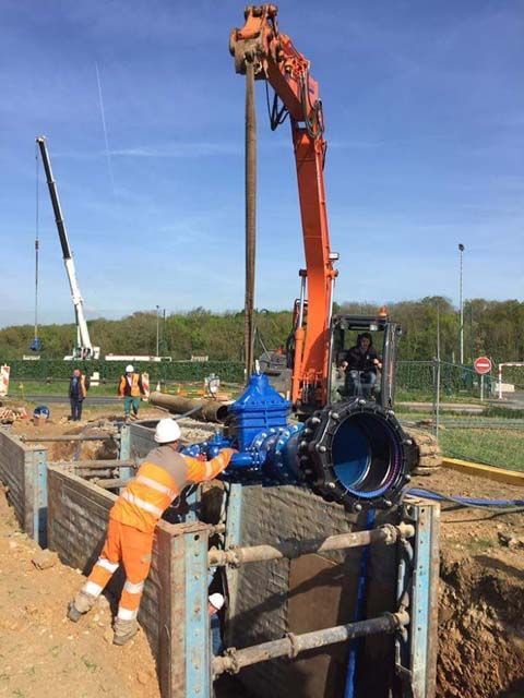 Des ouvriers du bâtiment installent une grande vanne bleue dans une tranchée à l'aide d'engins de chantier.