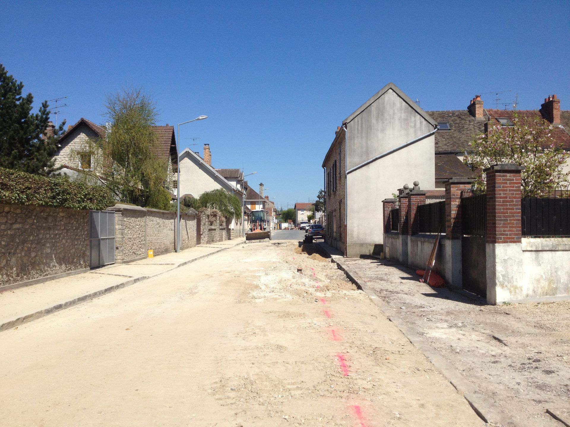 Travaux routiers dans une petite ville. La chaussée est décapée, les travaux sont en cours. Des bâtiments bordent la rue sous un ciel bleu.
