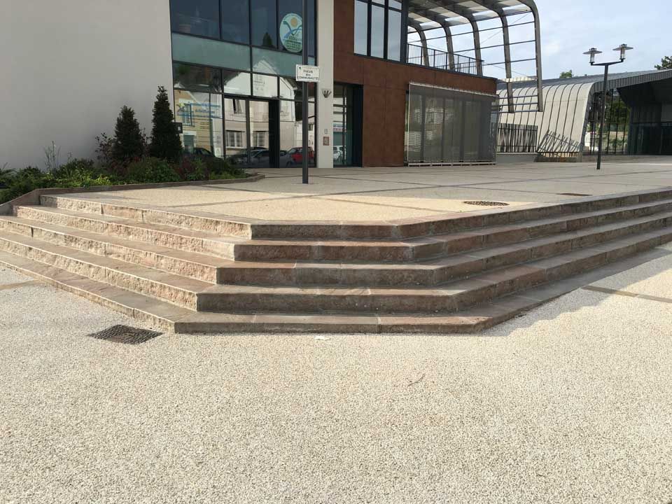 Vue extérieure des escaliers menant à un bâtiment moderne avec des fenêtres en verre, des touches de brun et une cour pavée.