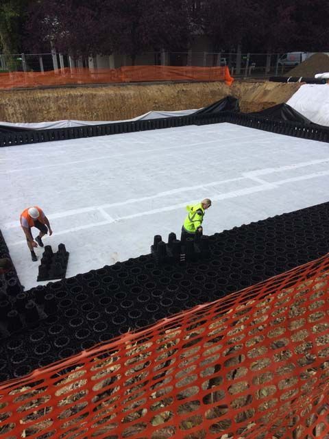 Deux ouvriers du bâtiment installent un système de drainage dans une grande excavation.