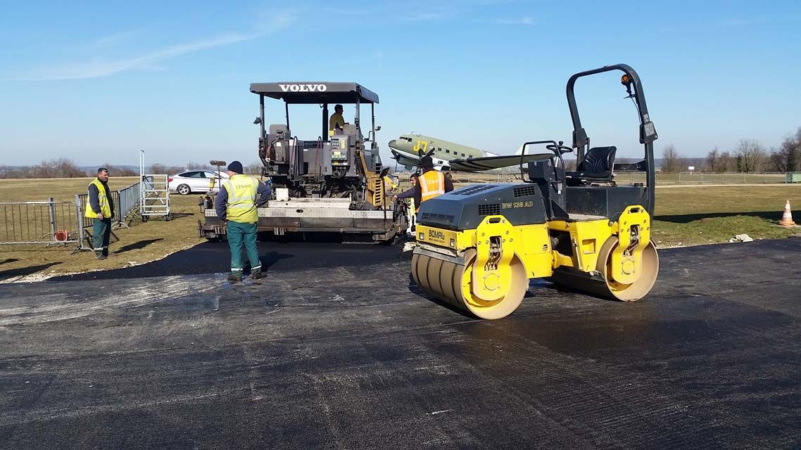 Travaux de pavage en cours : ouvriers, finisseur et rouleau compresseur jaune par une journée ensoleillée.