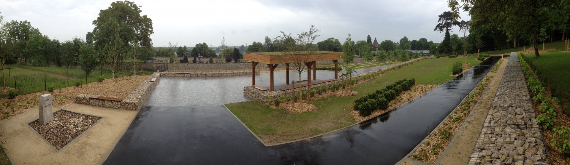 Vue panoramique pittoresque d'un parc avec un bassin réfléchissant et une pergola sous un ciel nuageux.