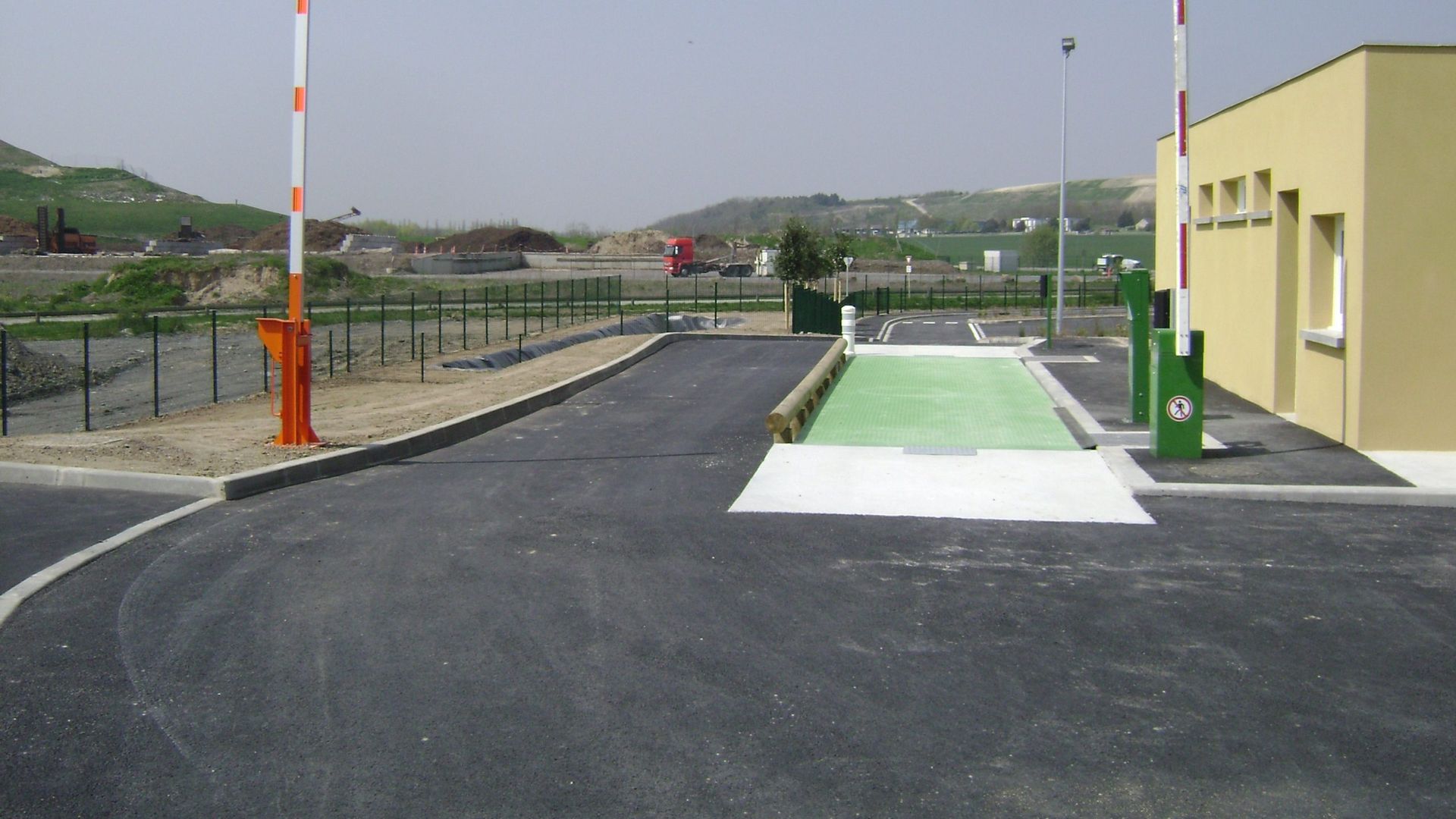 Un pont-bascule à l'entrée d'une installation, avec des barrières et un petit bâtiment.