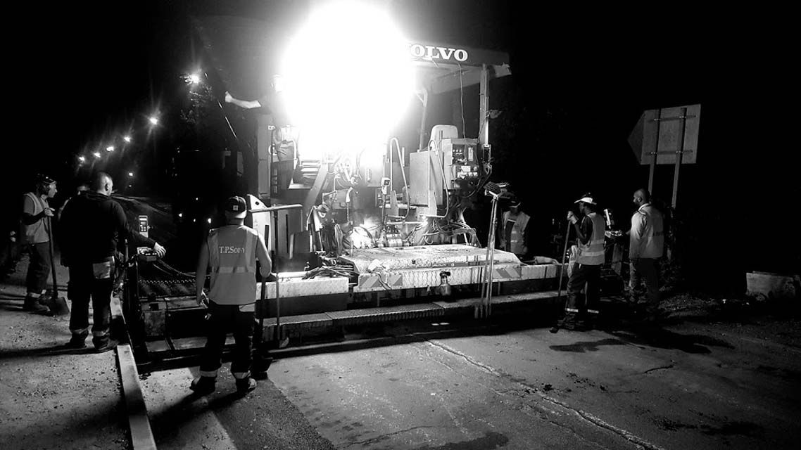 Travaux de pavage nocturnes, avec des projecteurs puissants illuminant les ouvriers et les engins.