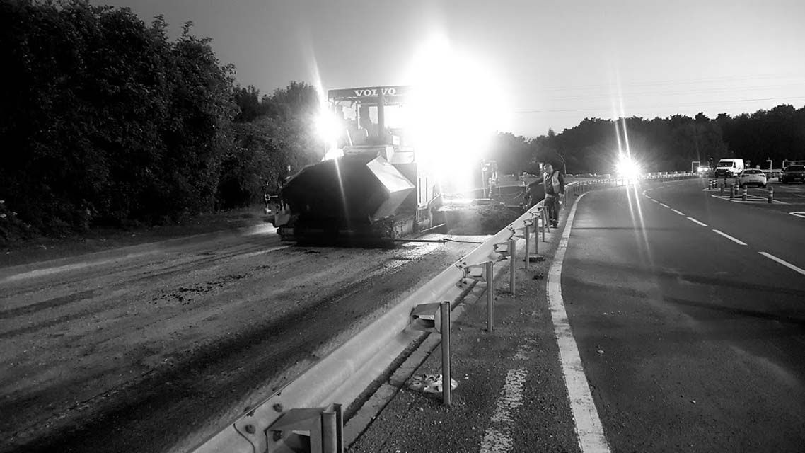 Une fraiseuse d'asphalte travaille de nuit sur une autoroute, éclairée par des projecteurs puissants.