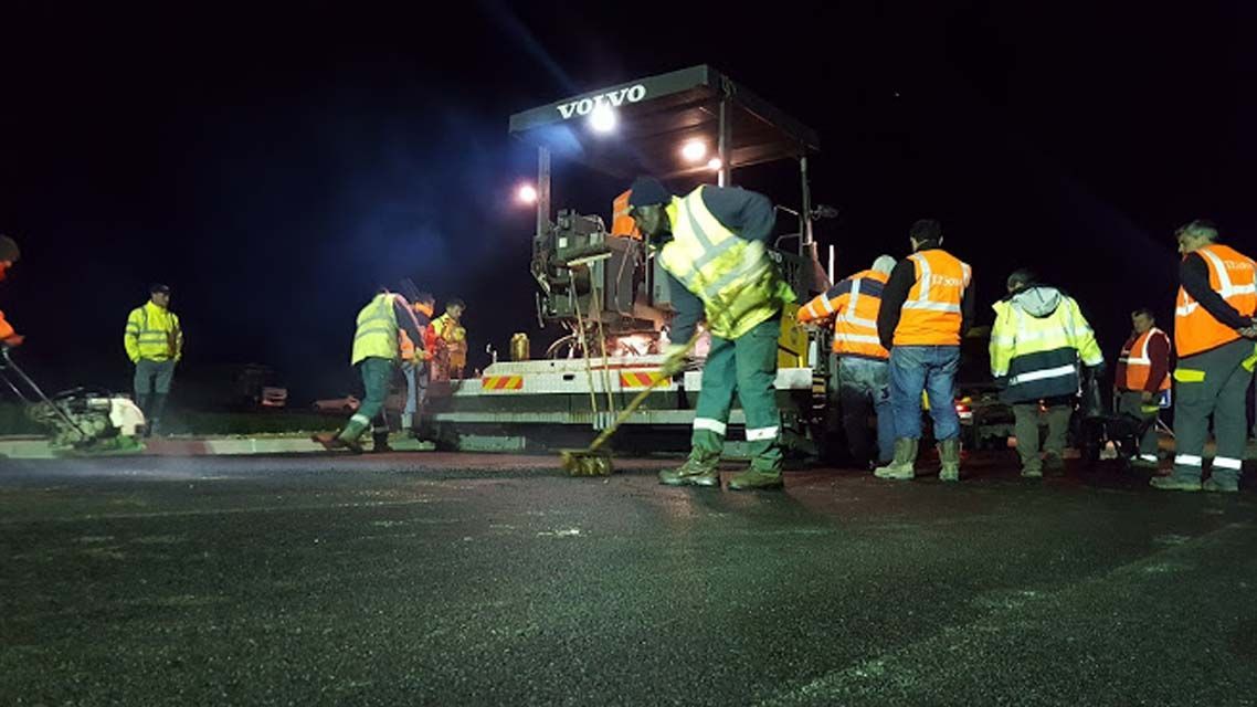 Des ouvriers routiers posent de l'asphalte de nuit, portant des gilets réfléchissants.