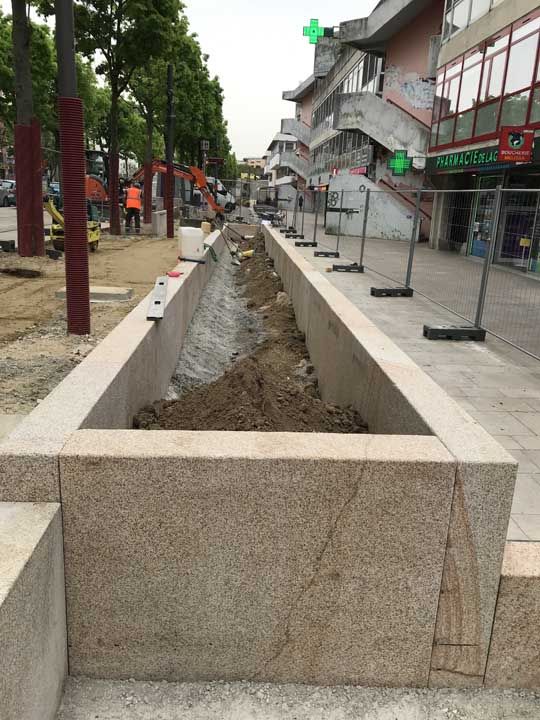 Travaux de voirie ; longue tranchée en pierre en cours de construction. Panneau vert de pharmacie et engins de chantier visibles.