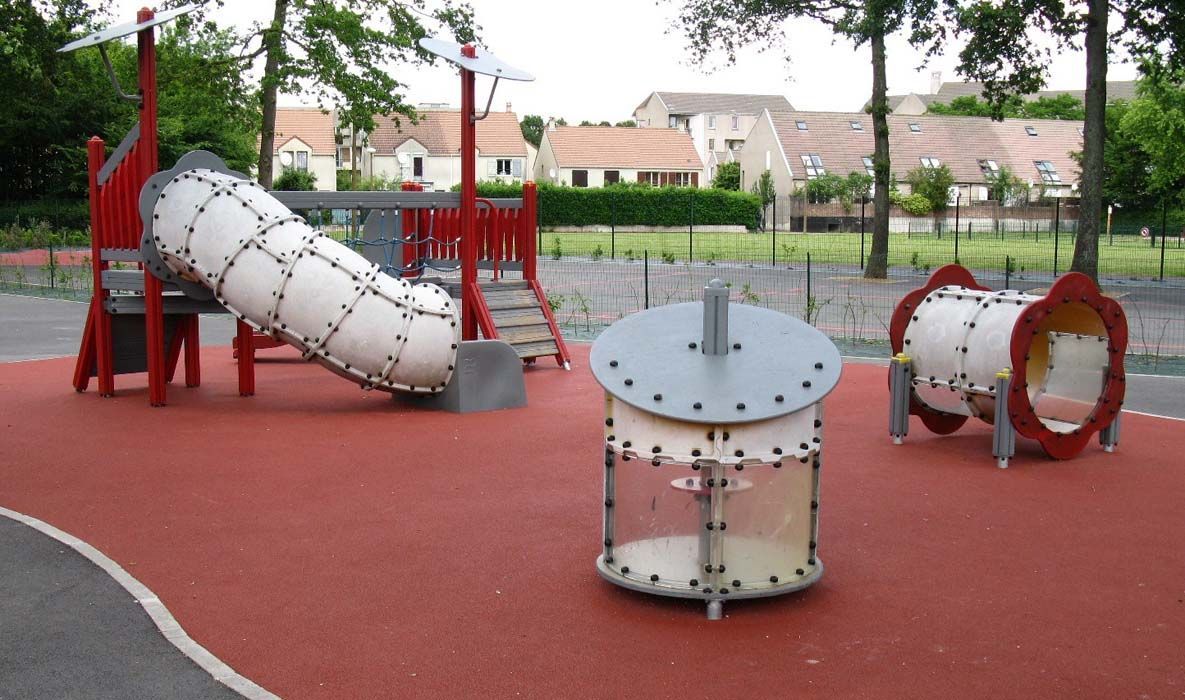 Aire de jeux avec revêtement de sécurité rouge, toboggans, tunnels et structure d'escalade.