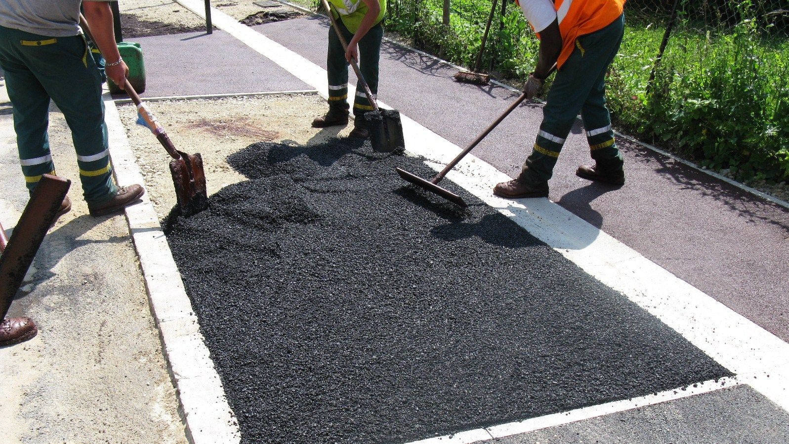 Des ouvriers recouvrent une portion de trottoir d'asphalte foncé.