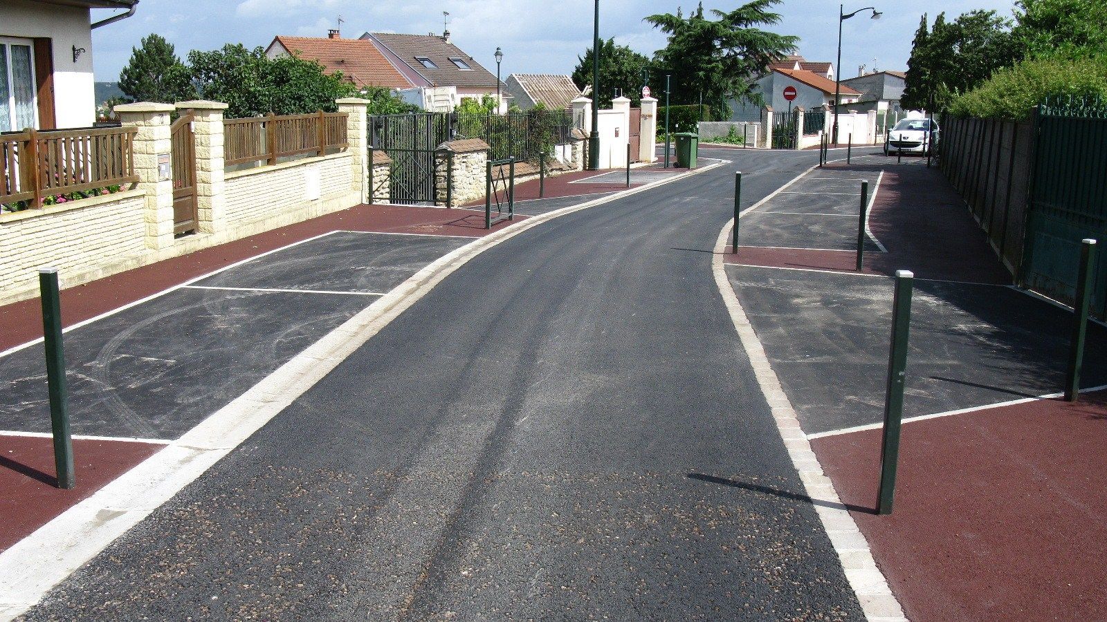 Route asphaltée bordée de rouge, de bornes vertes et de maisons en arrière-plan.