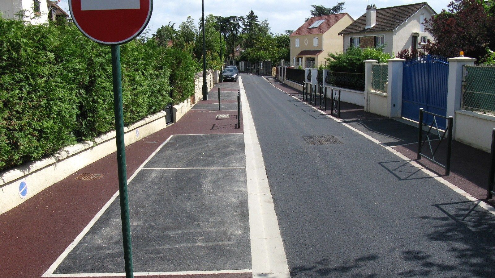 Route sans panneau d'interdiction d'entrée, passage piéton, trottoir, maisons des deux côtés, voiture garée au loin.