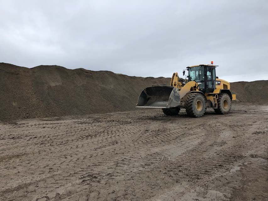 Une chargeuse frontale jaune est garée près d'un gros tas de gravier par temps nuageux.