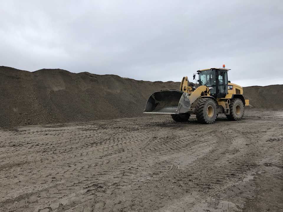 Une chargeuse frontale jaune ramasse du gravier d'un gros tas par temps nuageux.