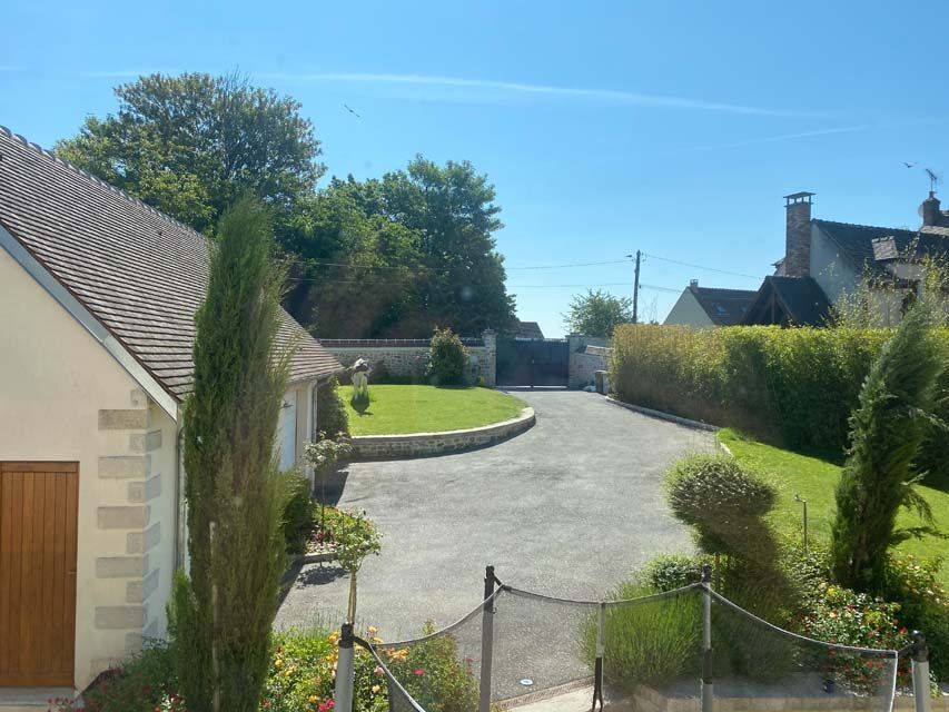 Allée menant à une maison avec pelouse verte, arbres et ciel bleu.
