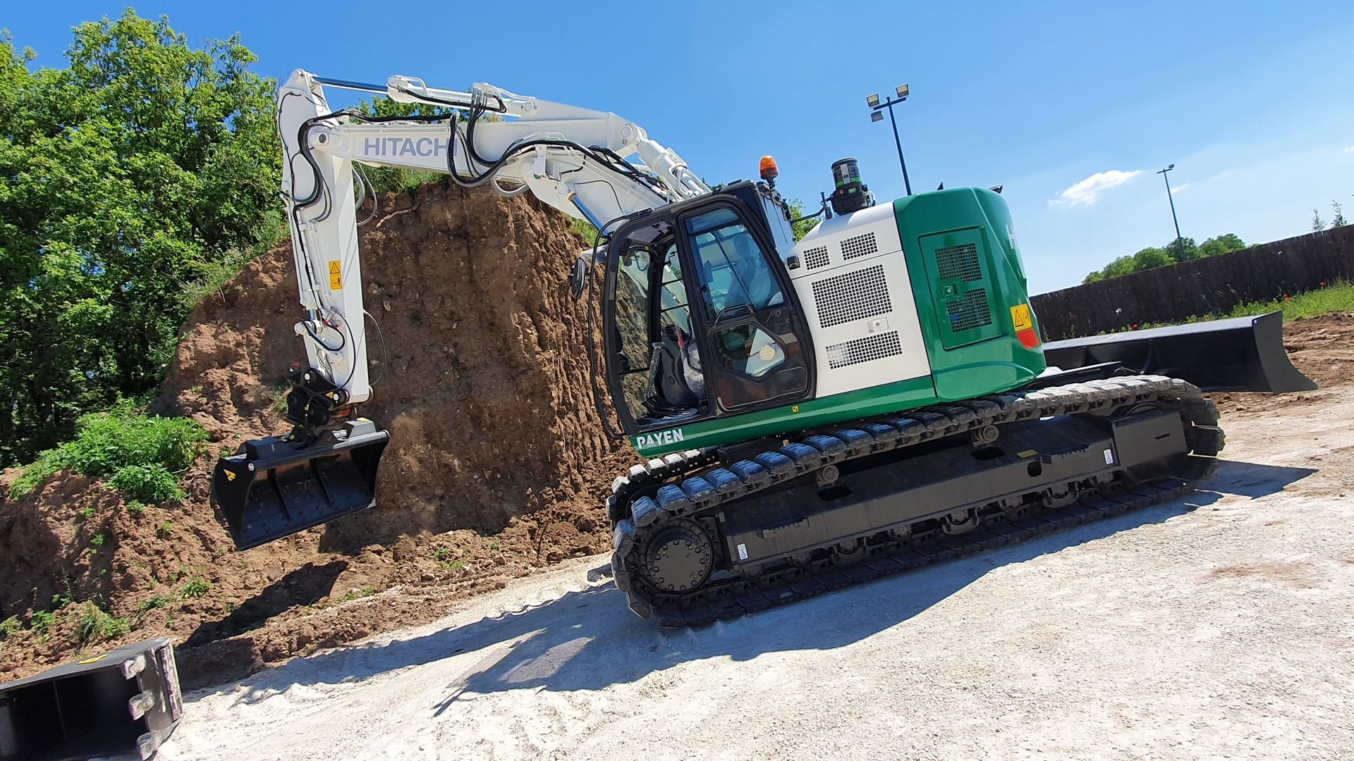 Une pelleteuse verte et blanche creuse un monticule de terre par une journée ensoleillée.