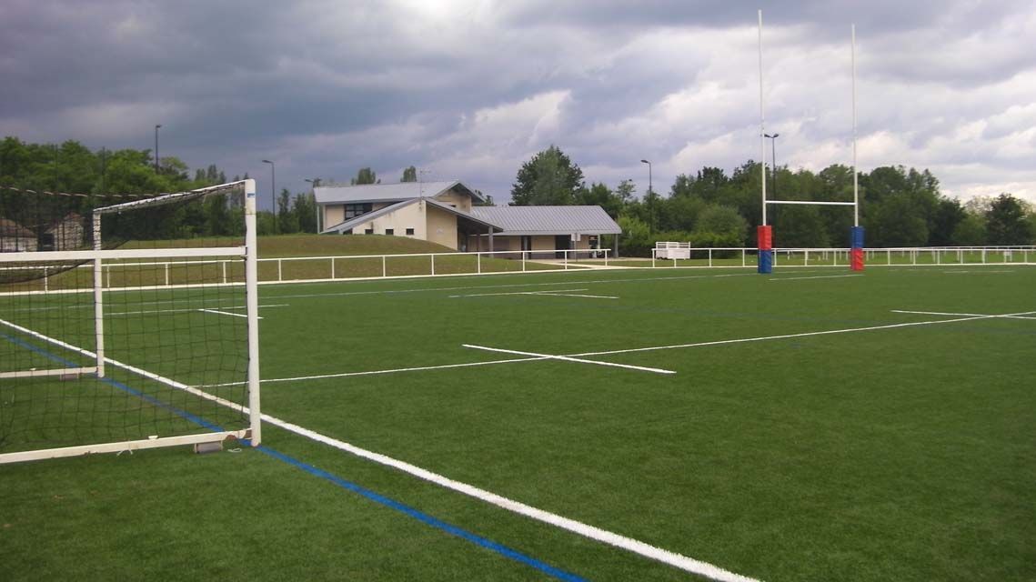 Terrain de rugby avec poteaux de but et un bâtiment sous un ciel couvert.